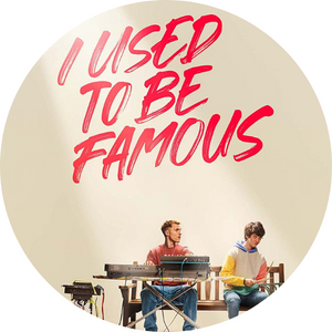 Promotional image for the Netflix movie called I Used To Be Famous. A musician sits on a park bench playing the keyboard in front of him white a young man with autism plays percussion on a green metal garbage can. Red text on the top of the image reads I Used To Be Famous.