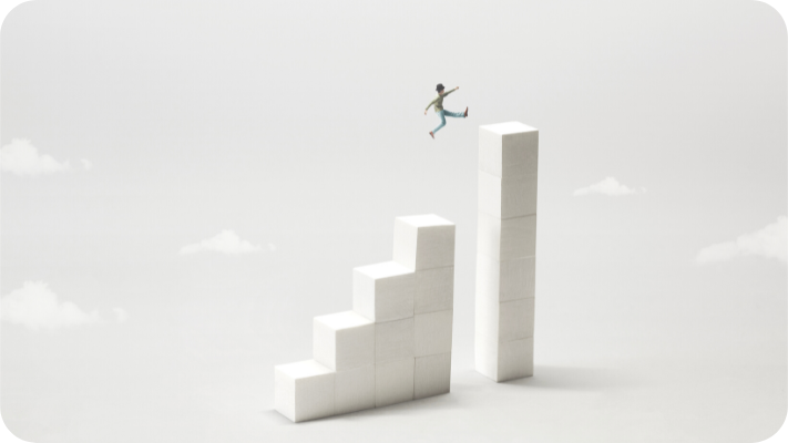 White cubes create steps in front of a light gray background with a few little clouds. A miniature clay figure is shown jumping across the gap between steps.